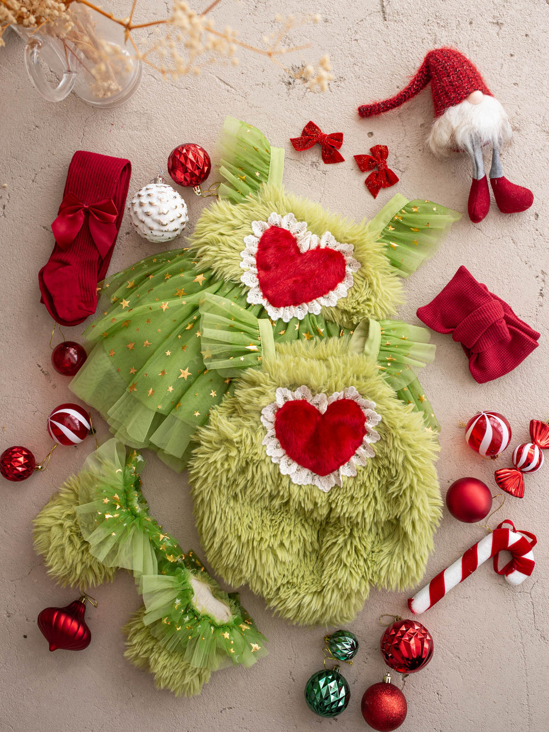 Miss Grump green tulle dress and Little Grump faux-fur romper laid out together for matching sisters, with red Christmas baubles, a candy cane and red bow tights - Before & Ever Kids