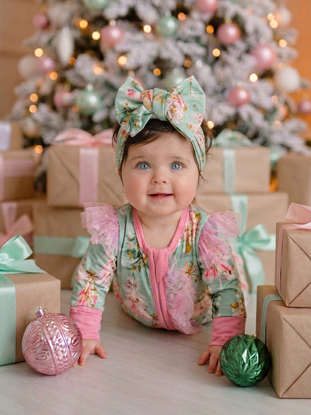 All I Wish Mint Pine baby onesie worn by a baby girl with the matching topknot headwrap, sitting in front of a Christmas tree with presents - Before & Ever Kids