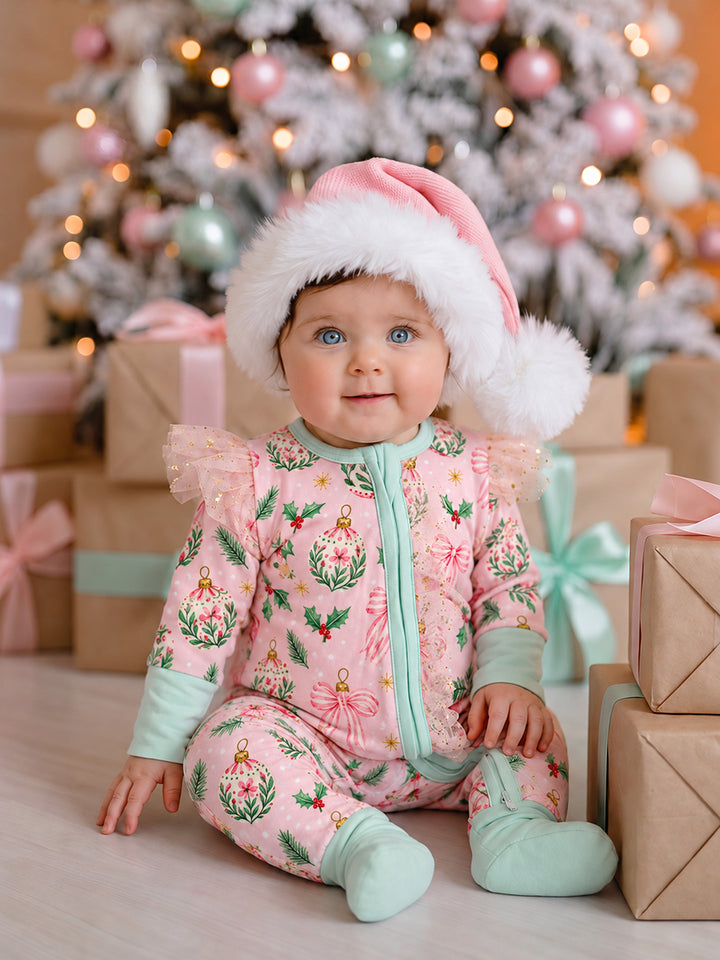 All I Wish Pink Holly baby onesie worn by a baby girl in a pink Santa hat, showing the holly, baubles and pink bow print with blush tulle flutter sleeves and mint cuffs - Before & Ever Kids