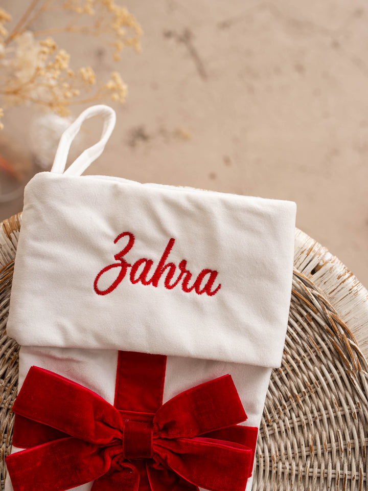 All Wrapped Up personalised Christmas stocking, close up of the white stocking's embroidered name and red velvet bow - Before & Ever Kids