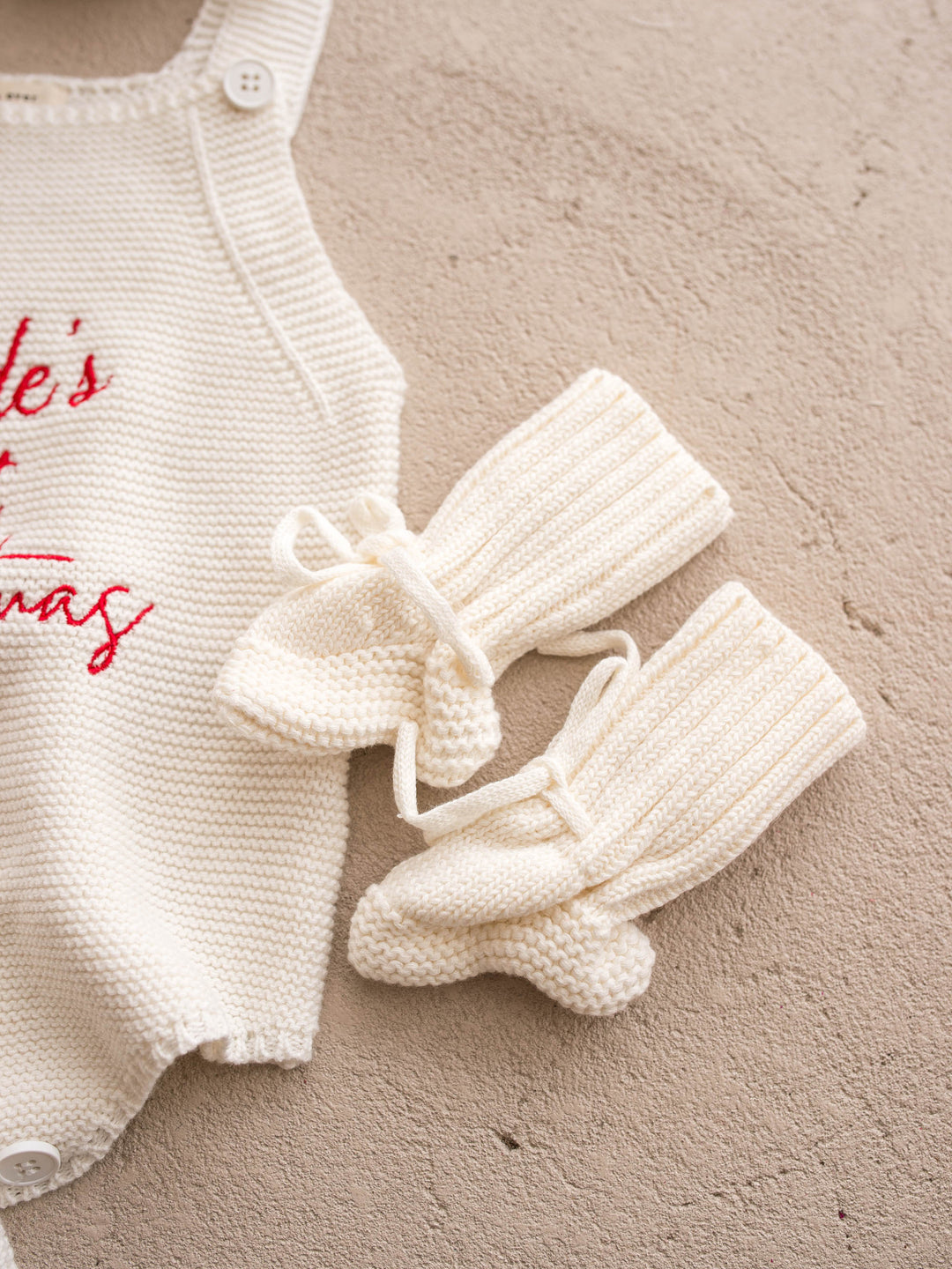Bliss Knitted Booties in milk cotton knit with ankle ties, flat beside a knit romper and baubles - Before & Ever Kids