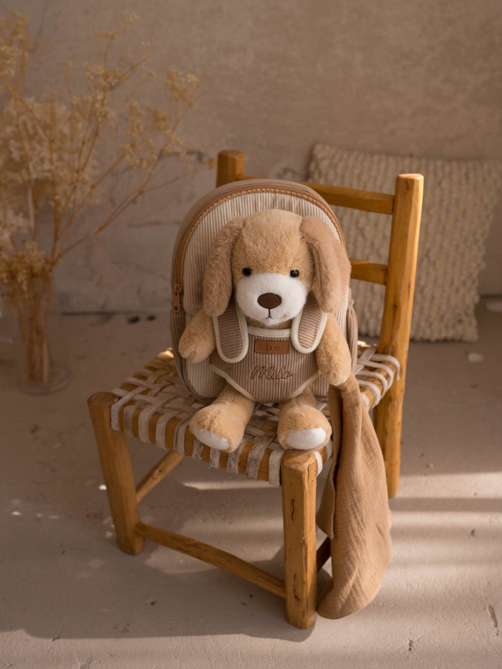 Milo the Puppy personalised plush backpack for kids, puppy sitting in the backpack on a chair - Before & Ever Kids