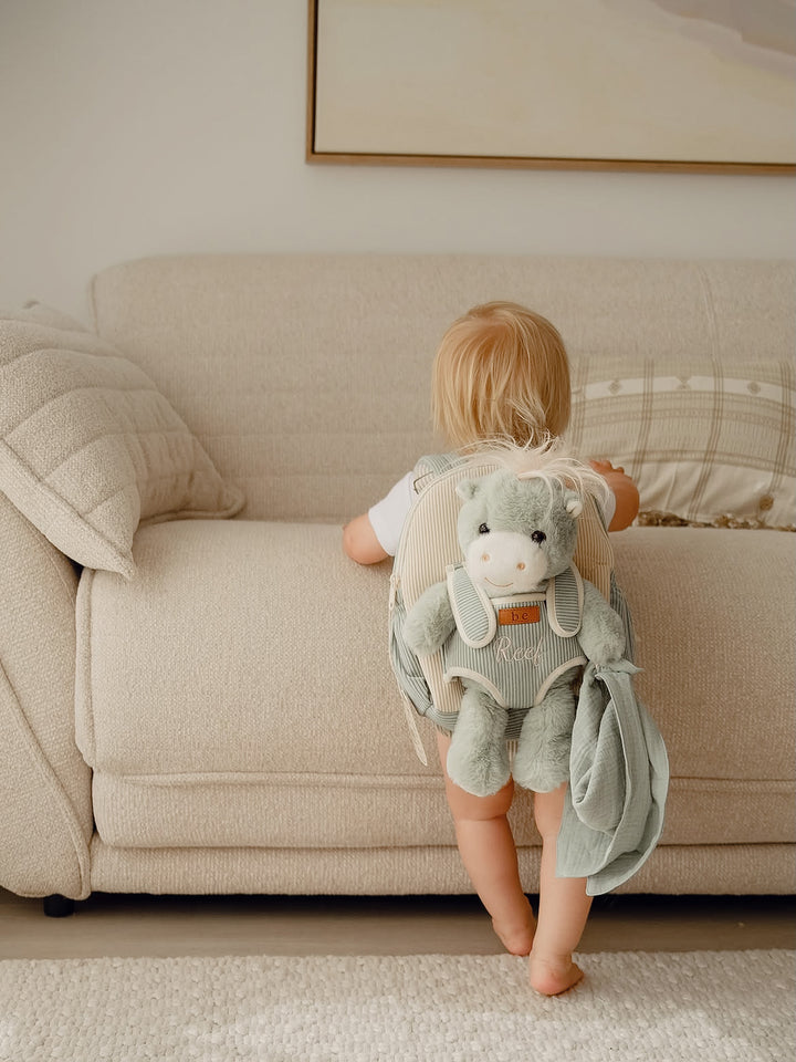 Sage the Horse personalised Little BFF Companion Backpack, toddler standing at the sofa wearing the backpack with the horse plush on the front - Before & Ever Kids