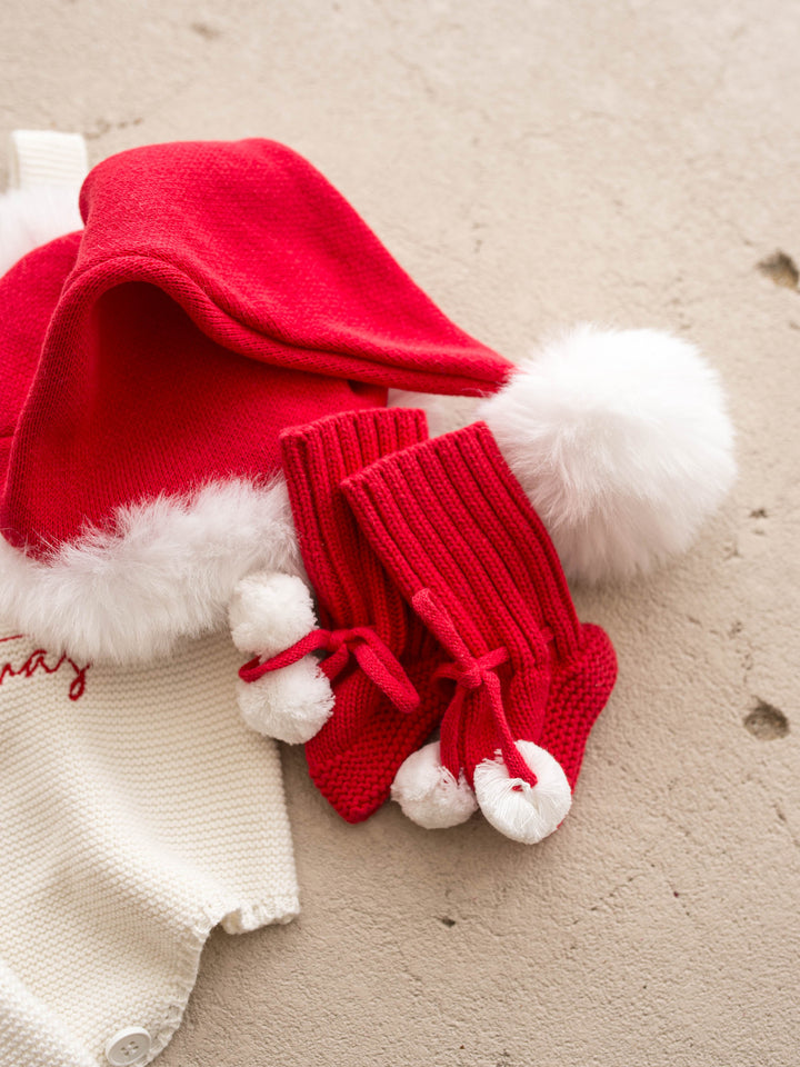 Santa Baby Knitted Booties in red cotton knit with white pom poms, with a red Santa hat and a cream knit romper - Before & Ever Kids
