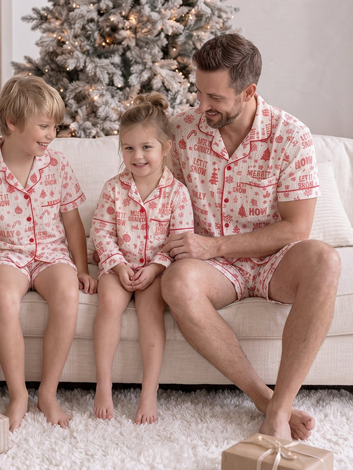 Twas the Night family Christmas pyjamas, white cotton muslin with a red Christmas print, dad in the short sleeve shirt and shorts on the sofa with the boy and girl - Before & Ever Kids