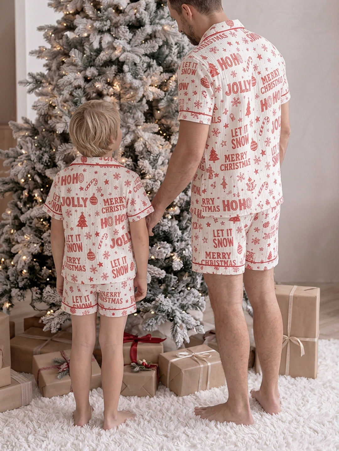 Twas the Night family Christmas pyjamas, white cotton muslin with a red Christmas print, dad and the boy standing by the tree in short sleeves and shorts, back view - Before & Ever Kids