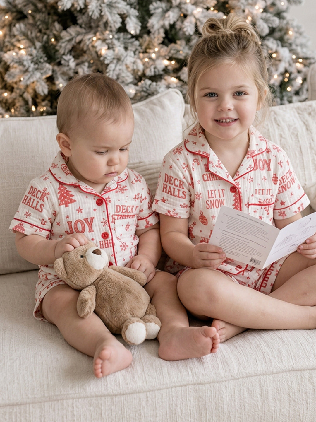 Twas the Night family Christmas pyjamas, white cotton muslin with a red Christmas print, baby and the girl sitting on the sofa in short sleeves reading a card - Before & Ever Kids