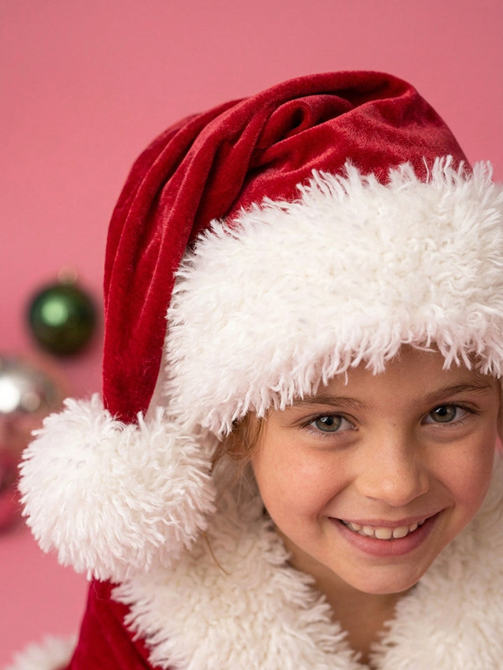 Velvet Santa Hat in deep red, worn by a smiling girl, big fluffy pom-pom at her shoulder - Before & Ever Kids