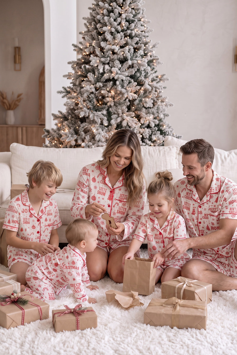 Family in matching Twas the Night Christmas pyjamas opening presents by the tree - Before & Ever Kids